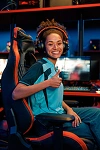 Młoda kobieta grająca w e-sport uśmiechająca się w profesjonalnym zestawie do gier z oświetleniem RGB i fotelem gamingowym.